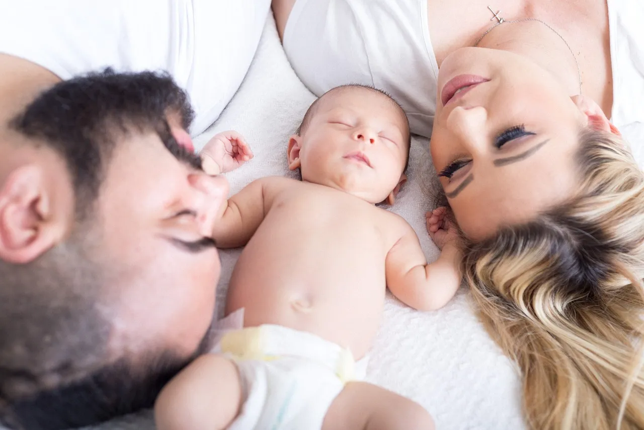 A headshot of couple lying down  with their new born baby in between their heads.