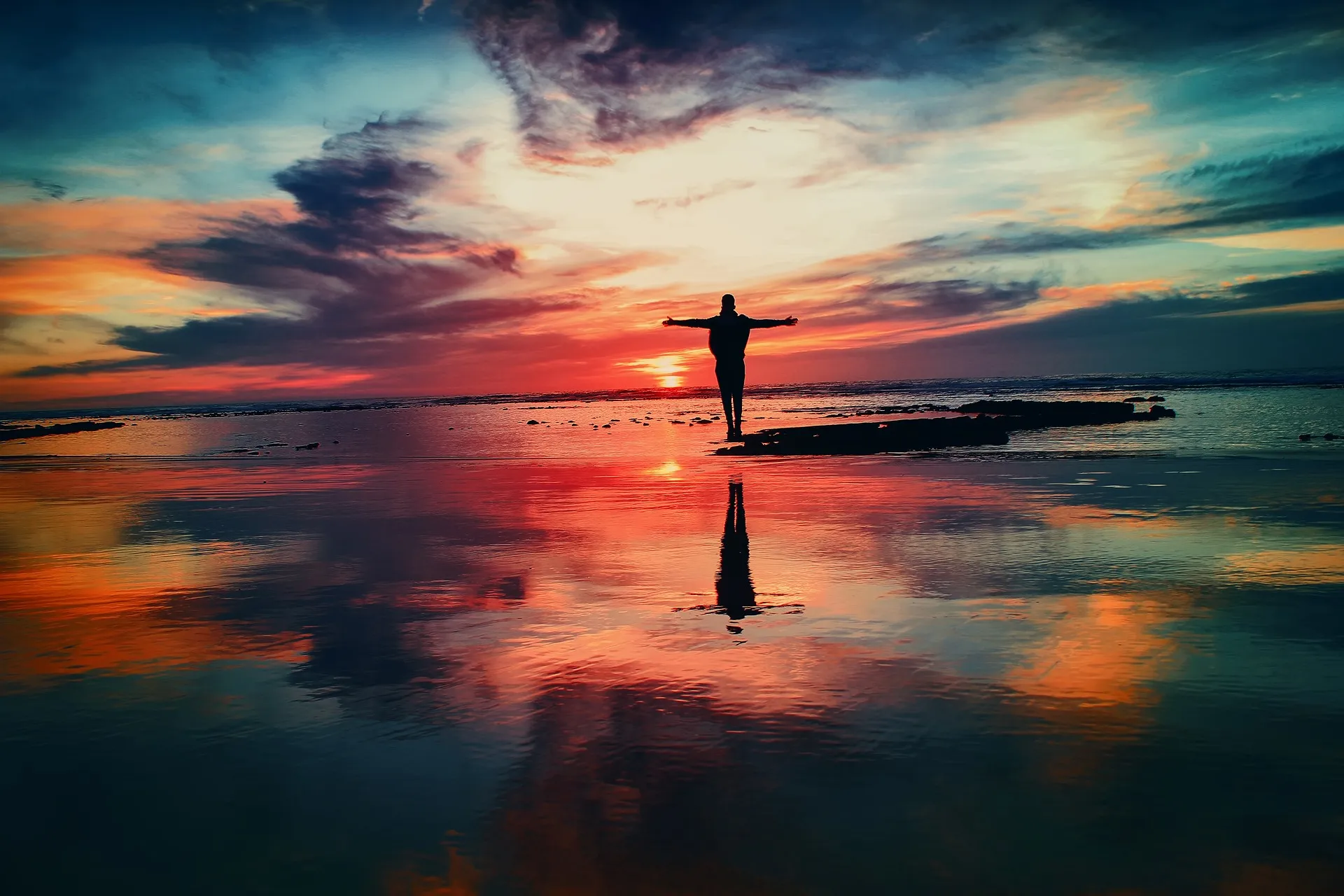 A person with their arms stretched out looking onto a sunset