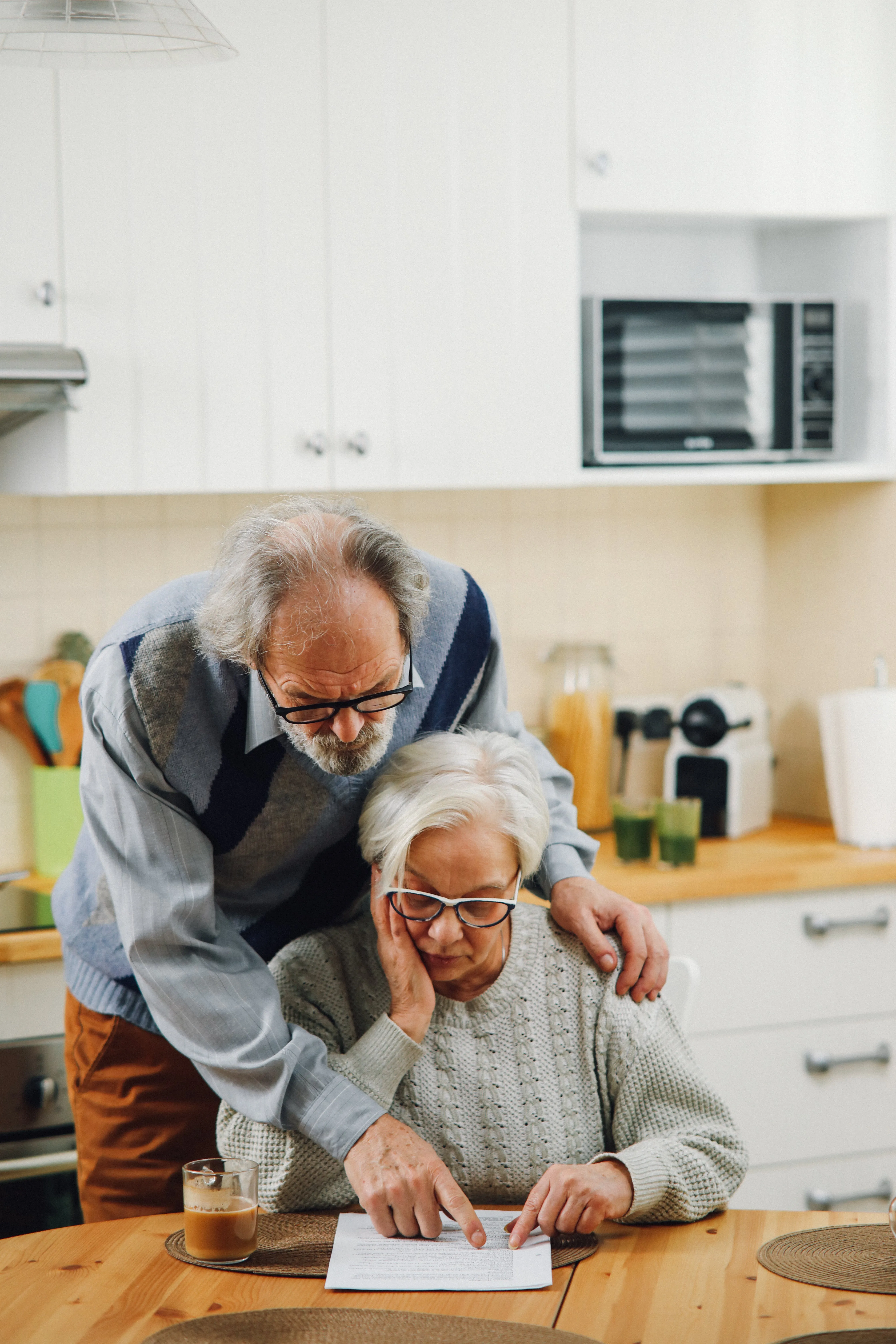 An elderly couple with the man standing and the woman sitting.